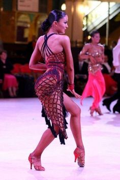 a woman in a red and black dress is dancing on the dance floor with other dancers behind her