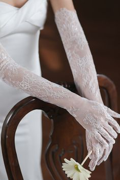 a woman wearing white gloves and holding a flower