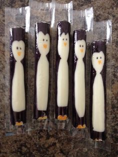 four penguin shaped candles sitting on top of a marble counter covered in plastic wrappers