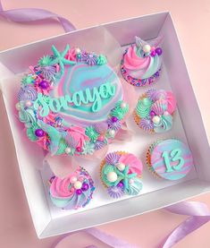 a box filled with cupcakes covered in frosting and colorful icing on top of a table