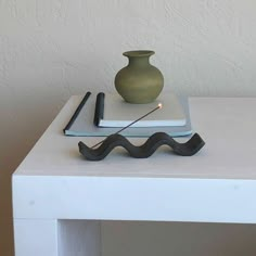 a white table topped with a book and a vase on top of it next to a pair of scissors