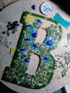 the letter b is made out of mosaic tiles and has blue flowers on it with green leaves