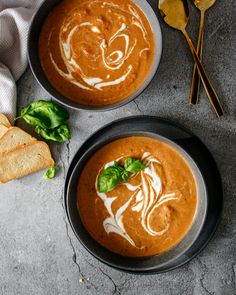 two bowls of tomato soup with bread and basil