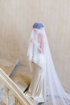 the bride is walking down the stairs in her wedding dress and veil over her head