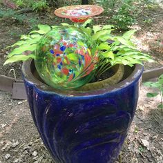 a blue planter with a glass ball in it and some plants growing out of it