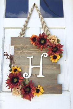 a wooden sign with flowers hanging from it's side and the letter h on top