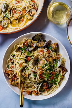 pasta with clams and vegetables in a bowl next to a glass of wine