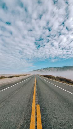 an empty road with yellow lines and clouds in the background