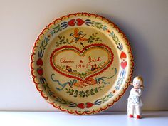 a small figurine stands next to a decorative plate with a heart on it