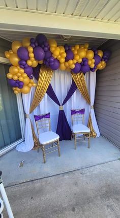 two chairs under a purple and gold balloon arch with white drapes on the sides