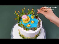 a cake decorated with ducks and plants on top of a white plate, in the shape of a pond