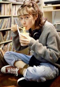 a young woman sitting on the floor eating food in front of a bookshelf