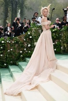 a woman in a long dress standing on some steps with people taking pictures behind her