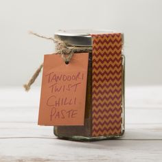 a jar filled with chili paste sitting on top of a white wooden table next to a tag