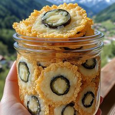 a person holding a jar filled with food on top of a wooden table next to mountains