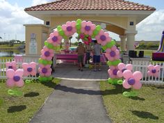 an archway decorated with pink and green flowers in front of a white fenced area