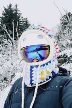 a person wearing ski goggles and a hat in front of snow - covered trees