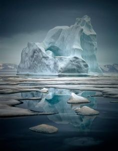 an iceberg floating in the water near some snow covered hills and mountains with dark clouds