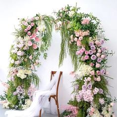 a chair sitting in front of a floral arch with pink and white flowers on it