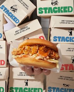 a person holding a sandwich in front of stacks of stacked boxes with stickers on them