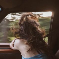 a woman sitting in the back seat of a car with her hair blowing in the wind