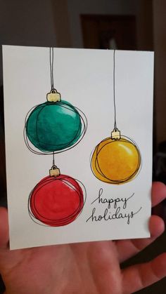 a hand holding up a card with three christmas ornaments hanging from it's sides