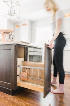 a woman standing next to an open cabinet in a kitchen