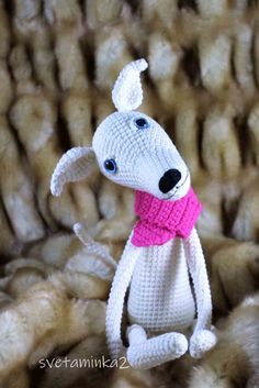 a crocheted dog with a pink scarf sitting in front of a pile of wool