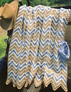 a crocheted blanket sitting on top of a wooden bench next to a hat