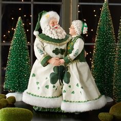 two figurines are dressed as santa claus and leprechaun in front of christmas trees