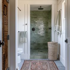 a bathroom with green tiles and a rug on the floor in front of the shower