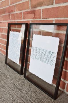 two black frames with white paper on them next to a brick wall and carpeted floor