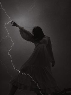 a woman in a white dress is holding her arm out as lightning strikes behind her