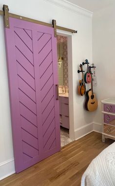 a bedroom with a purple door and guitars hanging on the wall next to the bed