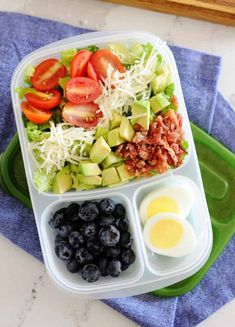 a salad in a plastic container with blueberries, avocado, and eggs