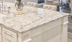 a kitchen island with marble counter tops and white chairs in the back drop off area