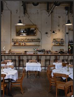 the interior of a restaurant with tables and chairs covered in white tablecloths, wine bottles on the wall