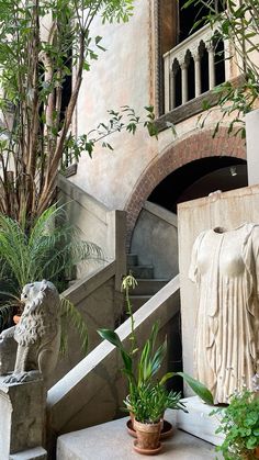 there is a statue in the middle of some plants and statues on the steps to a building