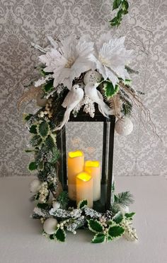 two candles are lit in front of a lantern with greenery and flowers on it