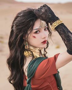 a woman with long hair wearing jewelry and holding her hand up to her head in the desert