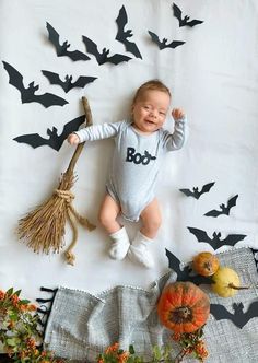 a baby laying on top of a white blanket next to pumpkins and bats hanging from the ceiling