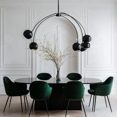 a dining room table with green chairs and a vase on the top, in front of a white paneled wall