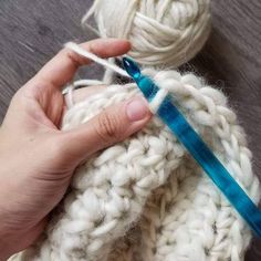 someone is crocheting together with yarn on the ground and one hand holding a blue handled knitting needle