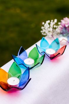 three colorful candles sitting on top of a table next to a vase filled with flowers