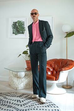 a man in a pink shirt and green suit standing next to a brown leather chair