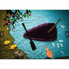 there is a purple umbrella and paddle on the ground next to some flowers, rocks and water