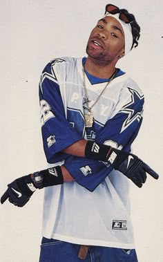 a young man with his arms crossed wearing gloves and a baseball cap, standing in front of a white background