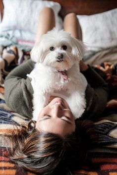 a woman laying on top of a bed with a white dog next to her face