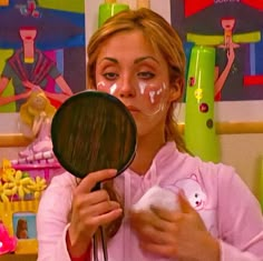 a woman holding a mirror in front of her face with white paint on it's cheek