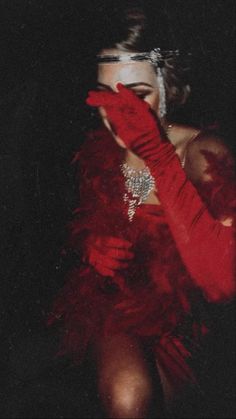 a woman in a red dress and feathered gloves is holding her hands up to her face